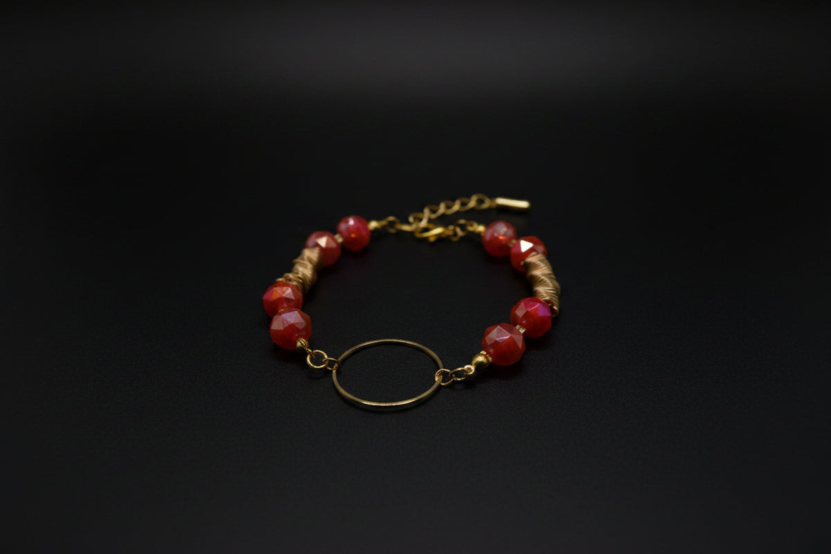 A gold-tone beaded bracelet with pink and red marbled beads, a textured gold spacer, and a central gold ring, displayed on a white background.
