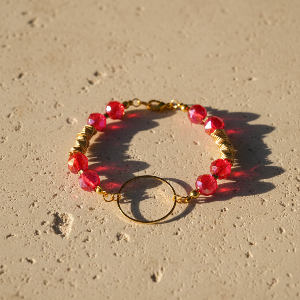 A beaded bracelet with pink and red marbled beads, gold-toned spacer links, and a central gold ring charm, displayed on a light gray background.