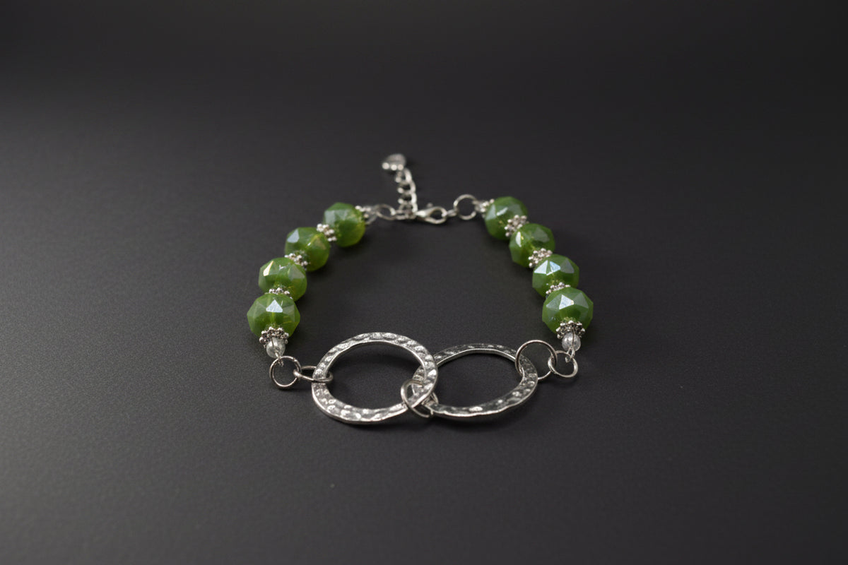 A beaded bracelet featuring green marbled beads, silver spacer rings, and a central double interlocking textured silver hoop clasp, displayed on a neutral gray background.