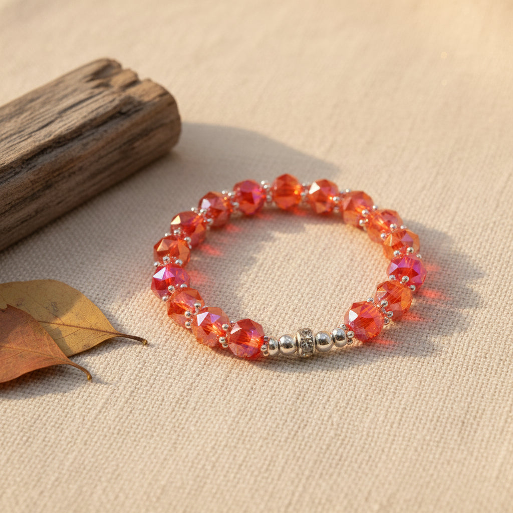 A beaded stretch bracelet featuring faceted orange and red beads with a metallic silver clasp, displayed on a plain light gray surface.