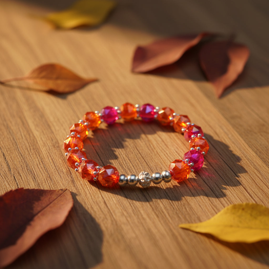 A beaded stretch bracelet featuring faceted orange and red beads with silver metallic accents, displayed on a plain light gray surface.