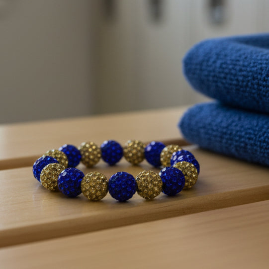 A beaded stretch bracelet featuring alternating royal blue and gold glittery faceted round beads, displayed on a neutral light gray background.