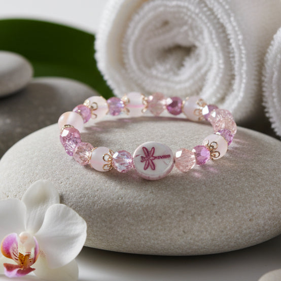 A beaded stretch bracelet featuring pink, purple, and iridescent beads, accented by two round white beads printed with a pink bow design, displayed on a neutral gray background.