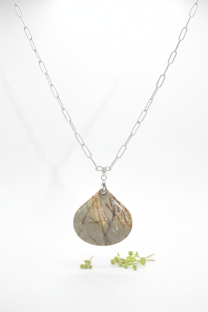 A silver chain necklace with a teardrop-shaped pendant made of polished stone showing brown and beige crystalline patterns, displayed on a black velvet jewelry bust.