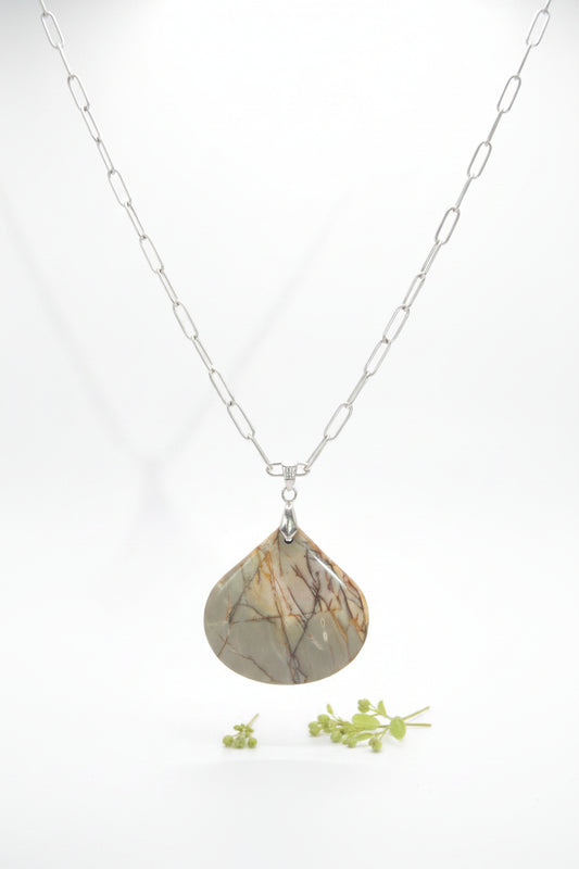 A silver chain necklace with a teardrop-shaped pendant made of polished stone showing brown and beige crystalline patterns, displayed on a black velvet jewelry bust.