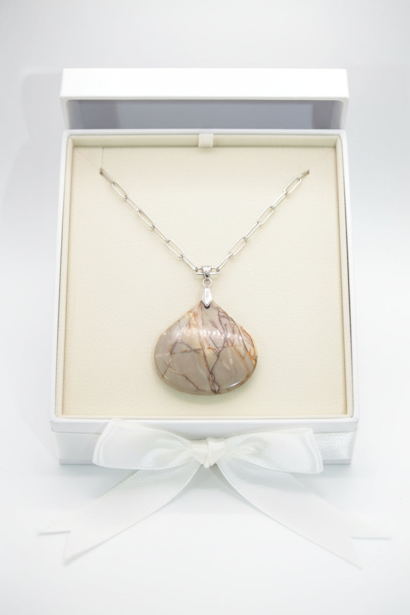 A silver chain necklace with a teardrop-shaped pendant made of polished brown and beige stone, displayed on a black velvet jewelry bust against a white background.