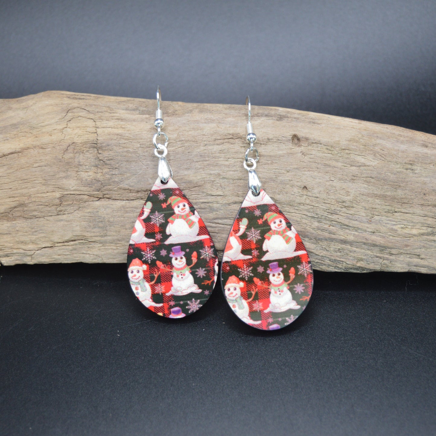 These cheerful teardrop earrings feature jolly snowmen nestled among red winter florals on a sleek black background. A festive blend of whimsy and elegance—perfect for cozy nights and holiday lights.