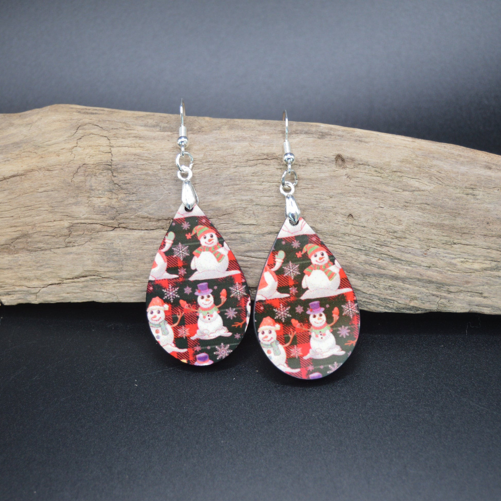These cheerful teardrop earrings feature jolly snowmen nestled among red winter florals on a sleek black background. A festive blend of whimsy and elegance—perfect for cozy nights and holiday lights.