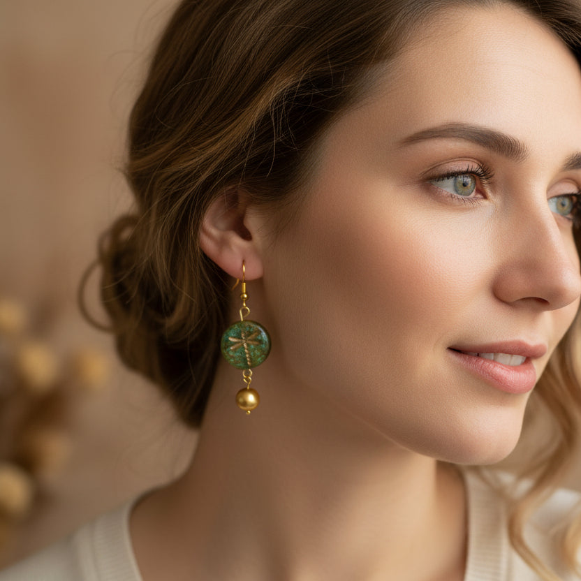 Pair of gold earrings with green and gold beads on a gray background
