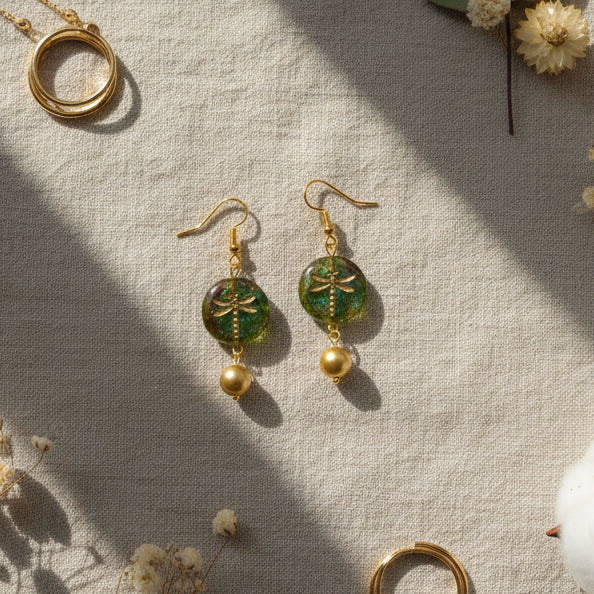 Gold earrings with green circular top and gold ball on a gray background