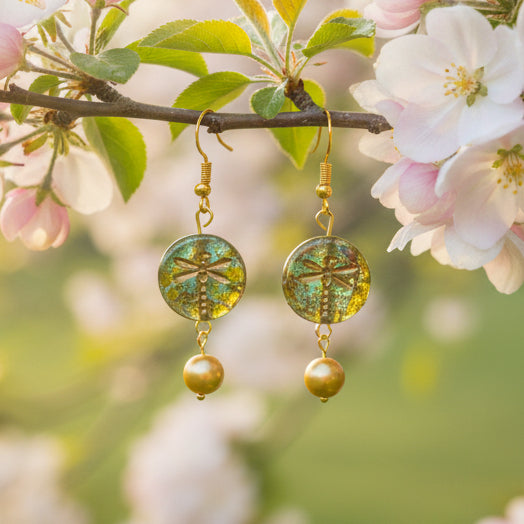 Pair of gold earrings with green and gold beads on a gray background