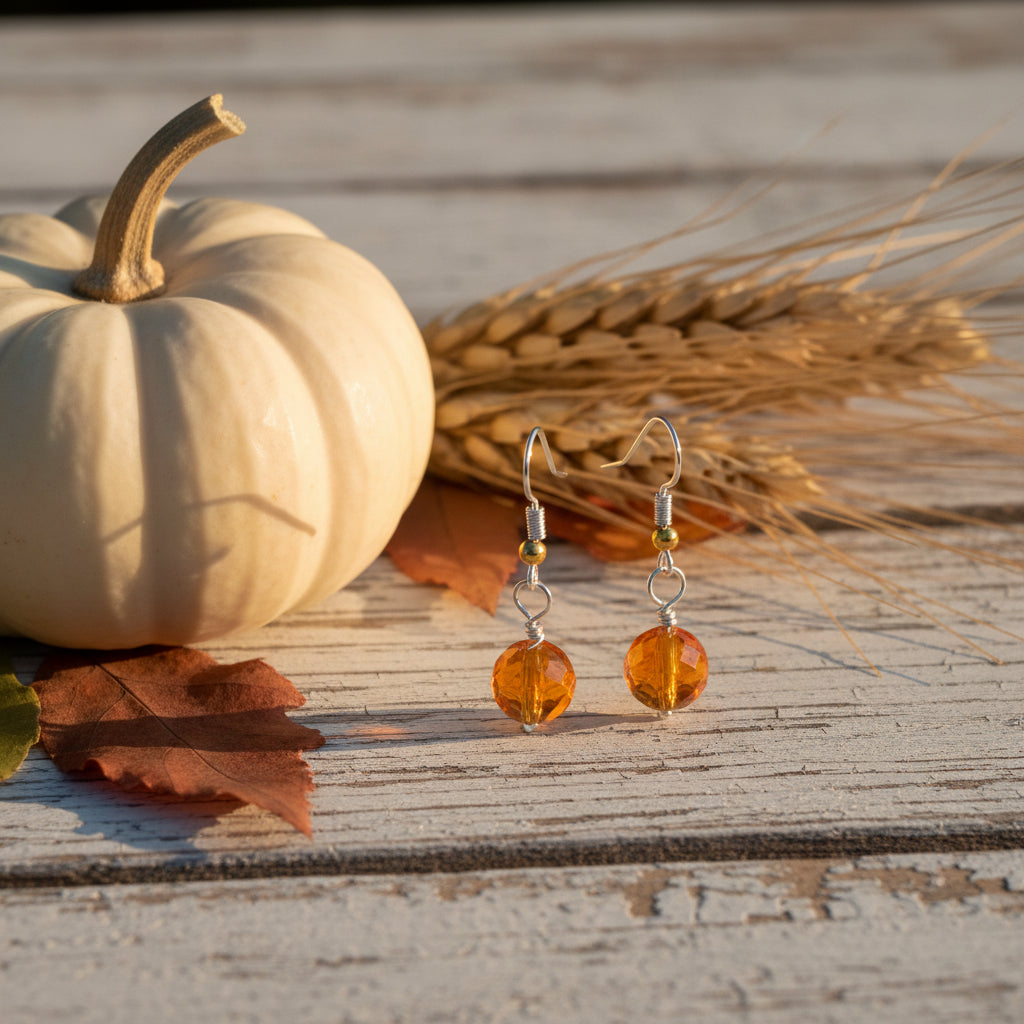 A pair of drop earrings with faceted orange beads and silver hooks, displayed on a clear plastic stand against a neutral gray background.