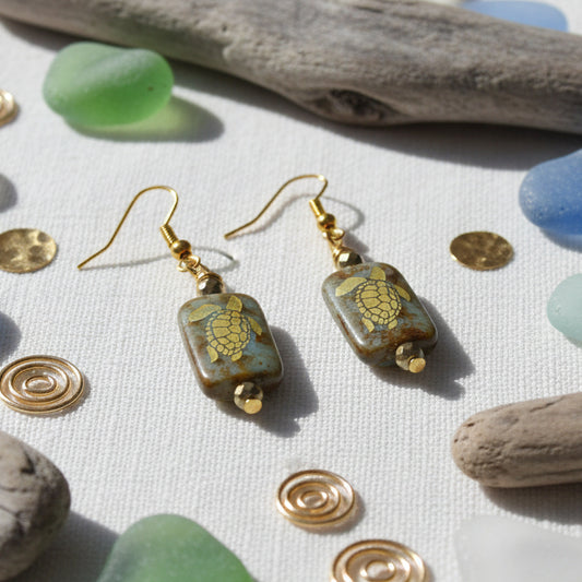 Pair of earrings with square beads featuring turtle design on a gray background