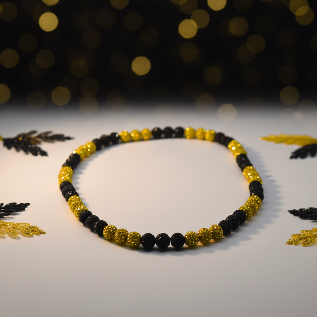 A beaded necklace with alternating sections of matte black faceted beads and metallic gold textured beads, arranged in an oval shape on a plain light gray background.