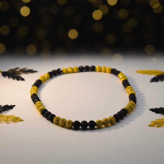 A beaded necklace with alternating sections of matte black faceted beads and metallic gold textured beads, arranged in an oval shape on a plain light gray background.