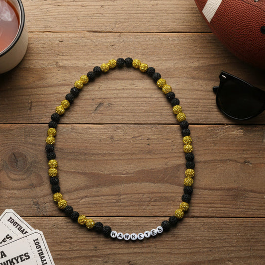 A beaded necklace with alternating black and yellow beads, featuring white letter beads spelling 'HAWKEYES' at the bottom, displayed on a white background.