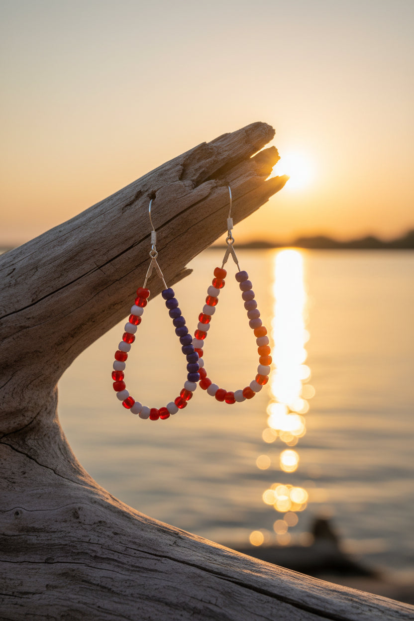 Beaded earrings on a piece of driftwood with a sunset over water background