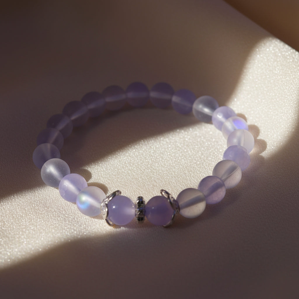 A beaded stretch bracelet featuring light purple and white beads, with a central cluster of round lavender beads and small silver spacer details, displayed on a neutral gray background.