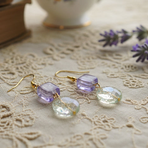 Pair of earrings with purple and clear beads on a gray background