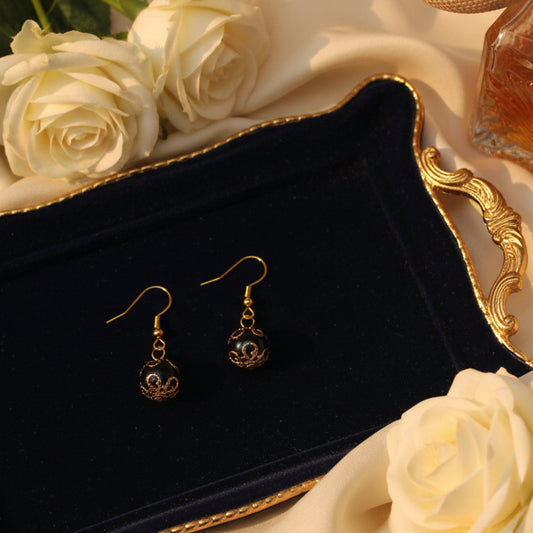 Pair of black and gold earrings on a clear stand against a gray background