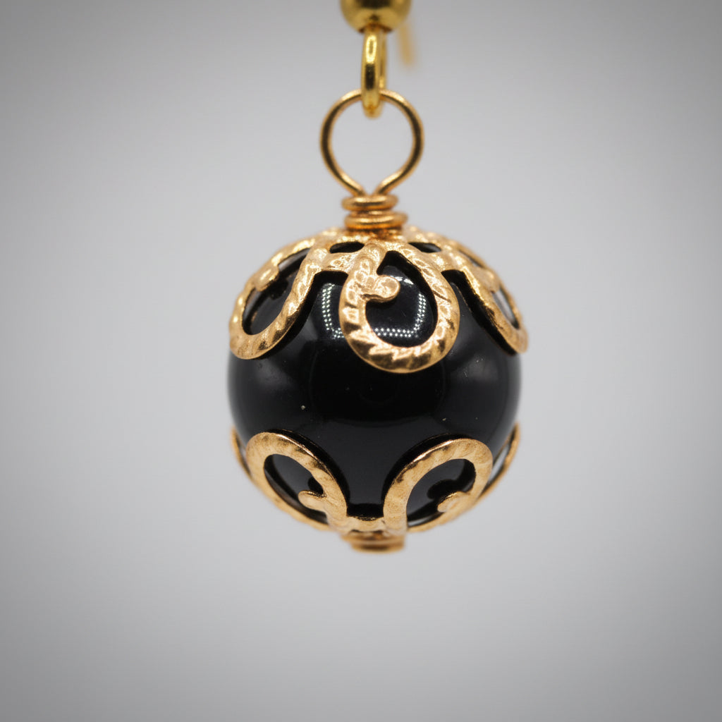 Pair of black and gold earrings on a clear stand against a gray background