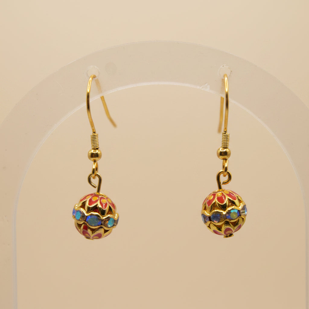 A pair of gold-tone dangle earrings with colorful enamel ball charms, displayed on a clear acrylic stand against a neutral gray background.