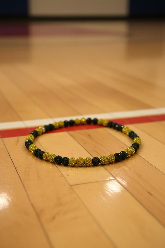 A beaded necklace with alternating black faceted beads and textured yellow beads, featuring a small beige stone accent bead, displayed on a plain light gray background.