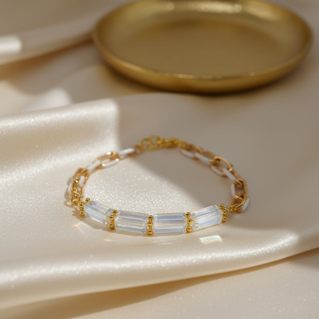 A gold chain bracelet featuring a central horizontal bar with four iridescent, clear glass beads set in gold, photographed on a plain light gray background.
