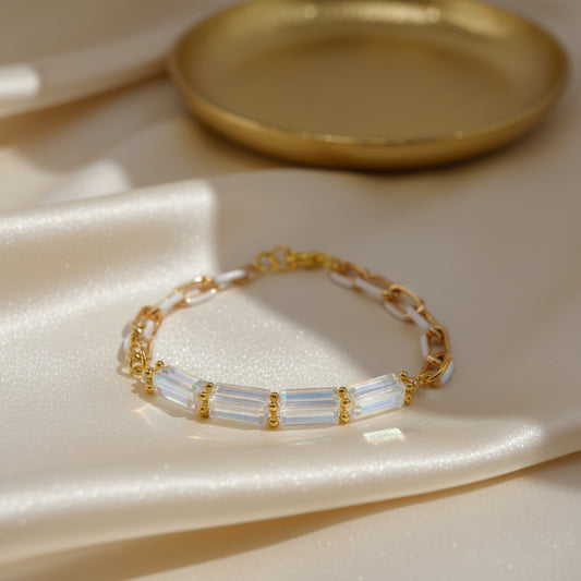 A gold chain bracelet featuring a central horizontal bar with four iridescent, clear glass beads set in gold, photographed on a plain light gray background.