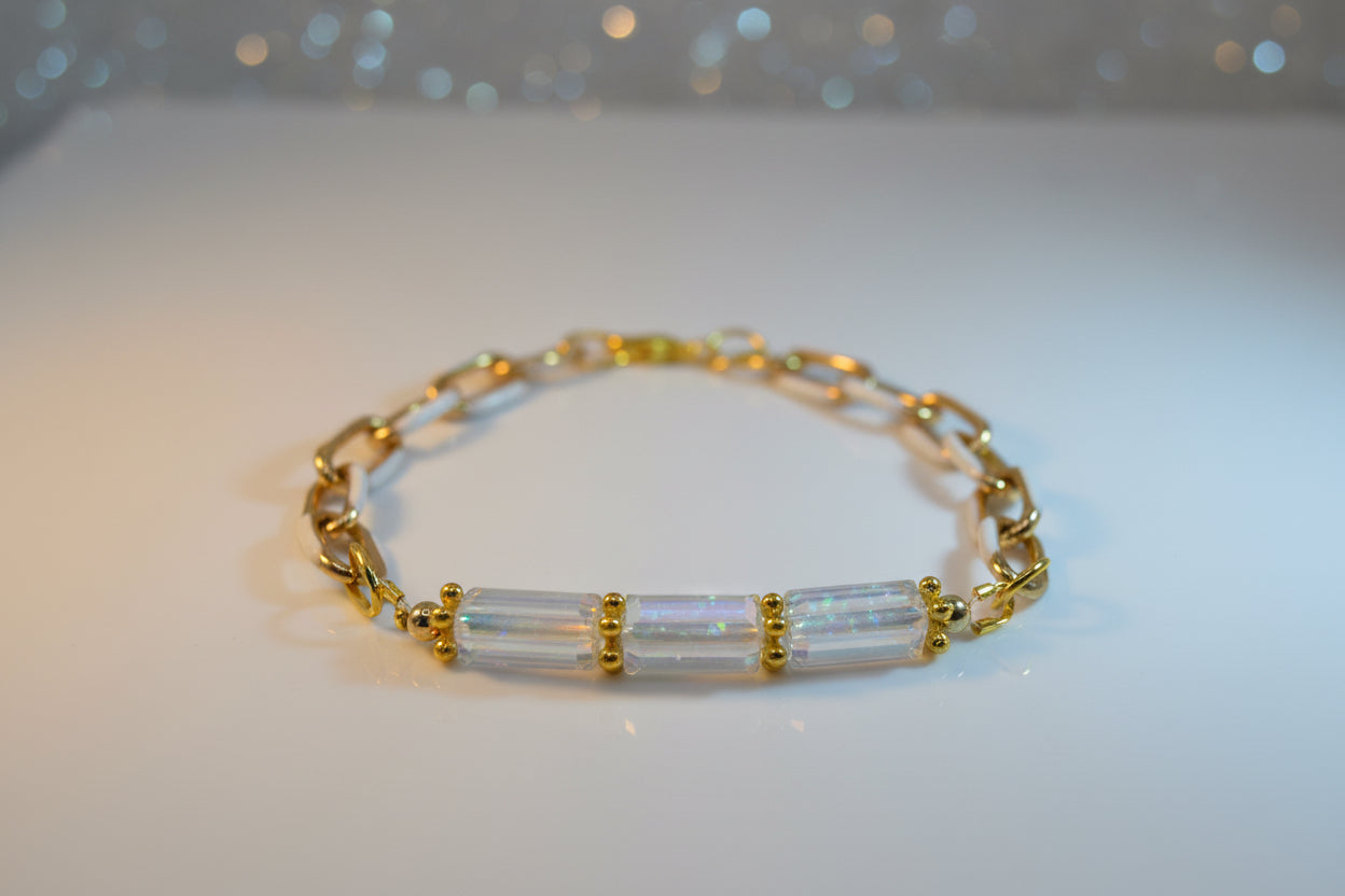 A gold chain bracelet featuring three rectangular iridescent glass beads on the front, set in gold-toned metal, photographed on a plain light gray background.