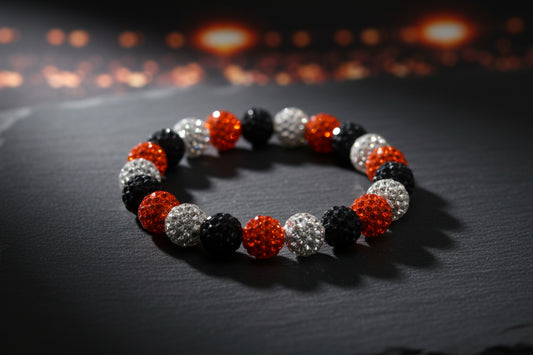 A beaded stretch bracelet featuring alternating black, orange, and silver rhinestone-covered round beads, displayed on a plain light gray background.