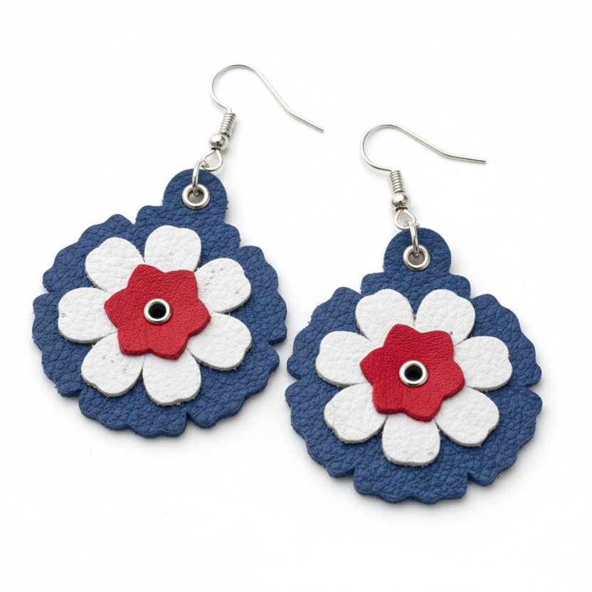Flower-shaped earrings with blue, red, and white colors on a dark surface next to a ruler.