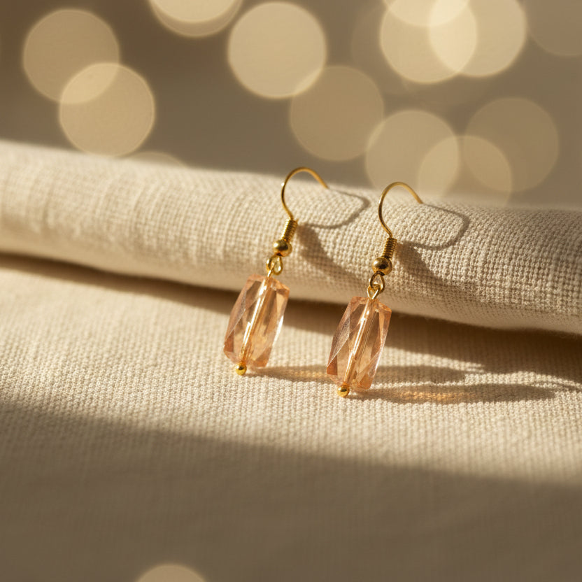 Pair of gold earrings with pink beads on a gray background