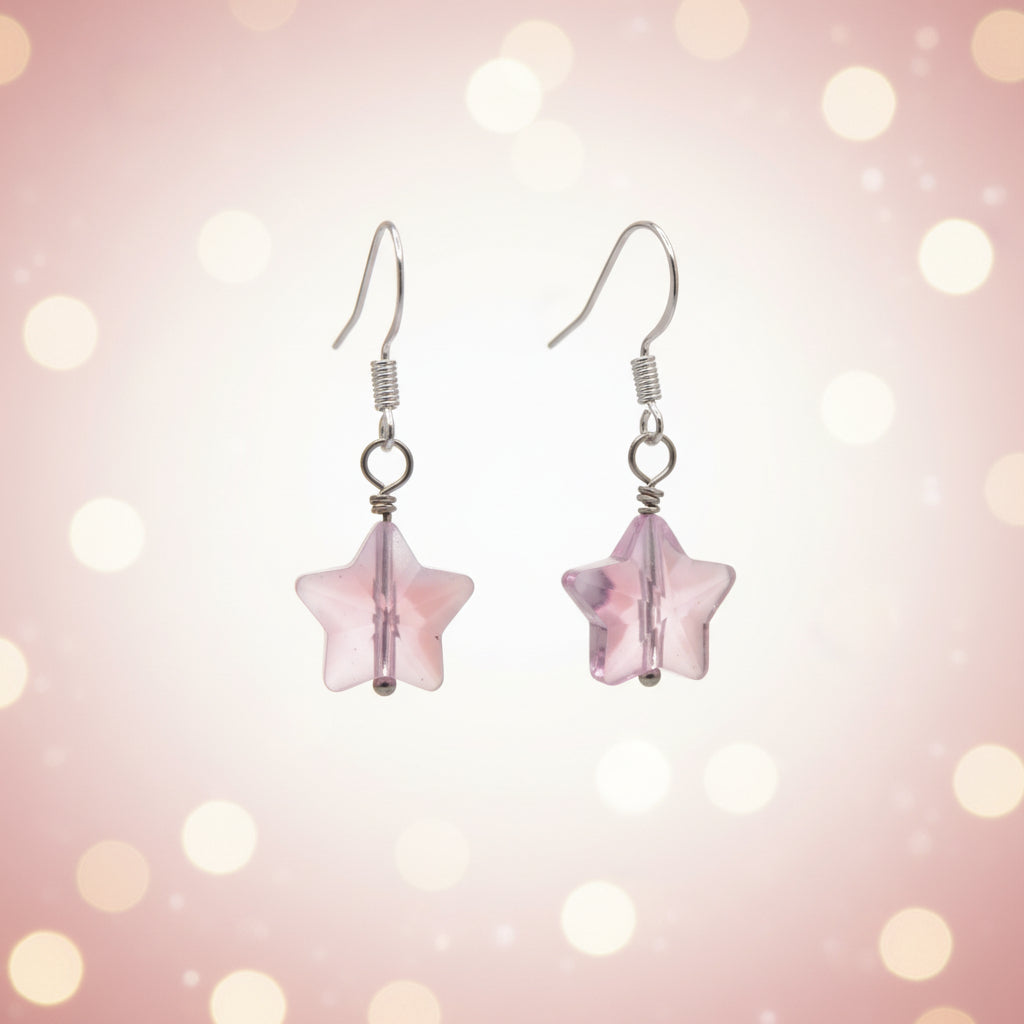 A pair of handmade dangle earrings featuring translucent light pink star-shaped beads suspended from silver-toned fishhook wires, displayed against a neutral gray background.