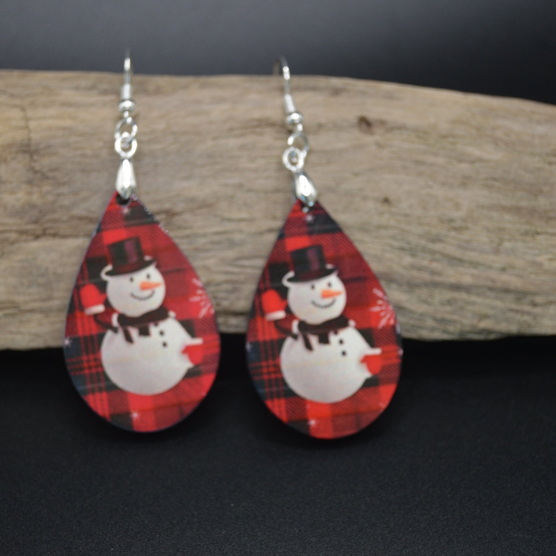 These teardrop earrings feature a dapper snowman in a top hat and scarf, set against a cozy red-and-black plaid backdrop. A charming blend of winter whimsy and rustic style—perfect for holiday gatherings and fireside fun.