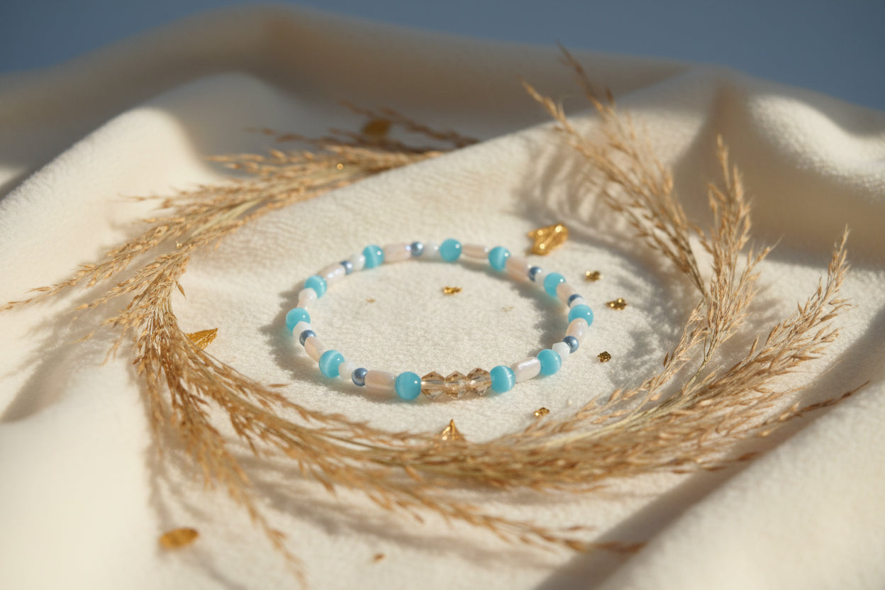 A beaded stretch bracelet featuring turquoise blue beads, white cylindrical beads, small metallic silver beads, and a central gold-toned link clasp, displayed on a neutral gray background.
