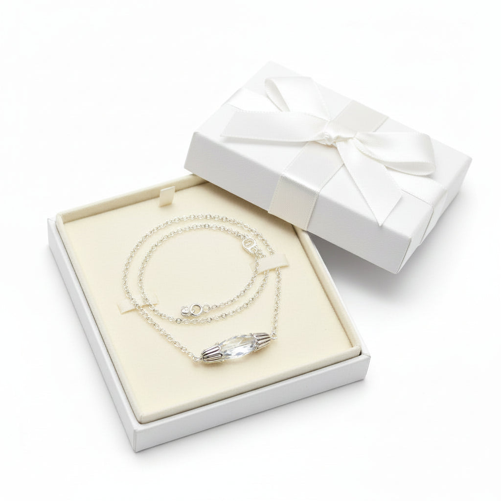 A silver chain necklace with a small silver-toned oval pendant displayed on a black velvet necklace bust against a white background.
