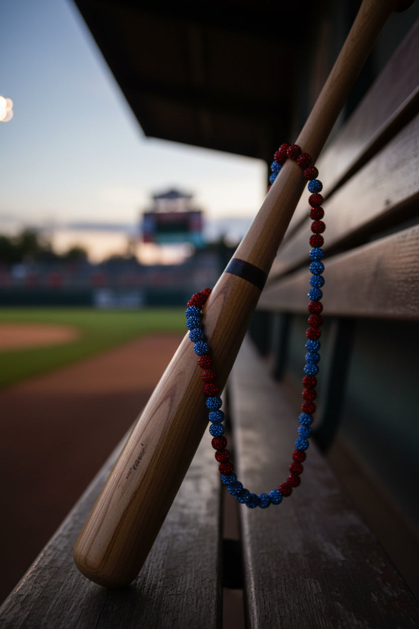 A beaded necklace made of alternating red and blue glittery round beads, arranged in an oval shape on a plain light gray surface.