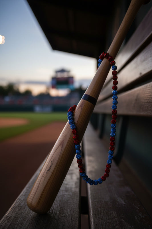 A beaded necklace made of alternating red and blue glittery round beads, arranged in an oval shape on a plain light gray surface.
