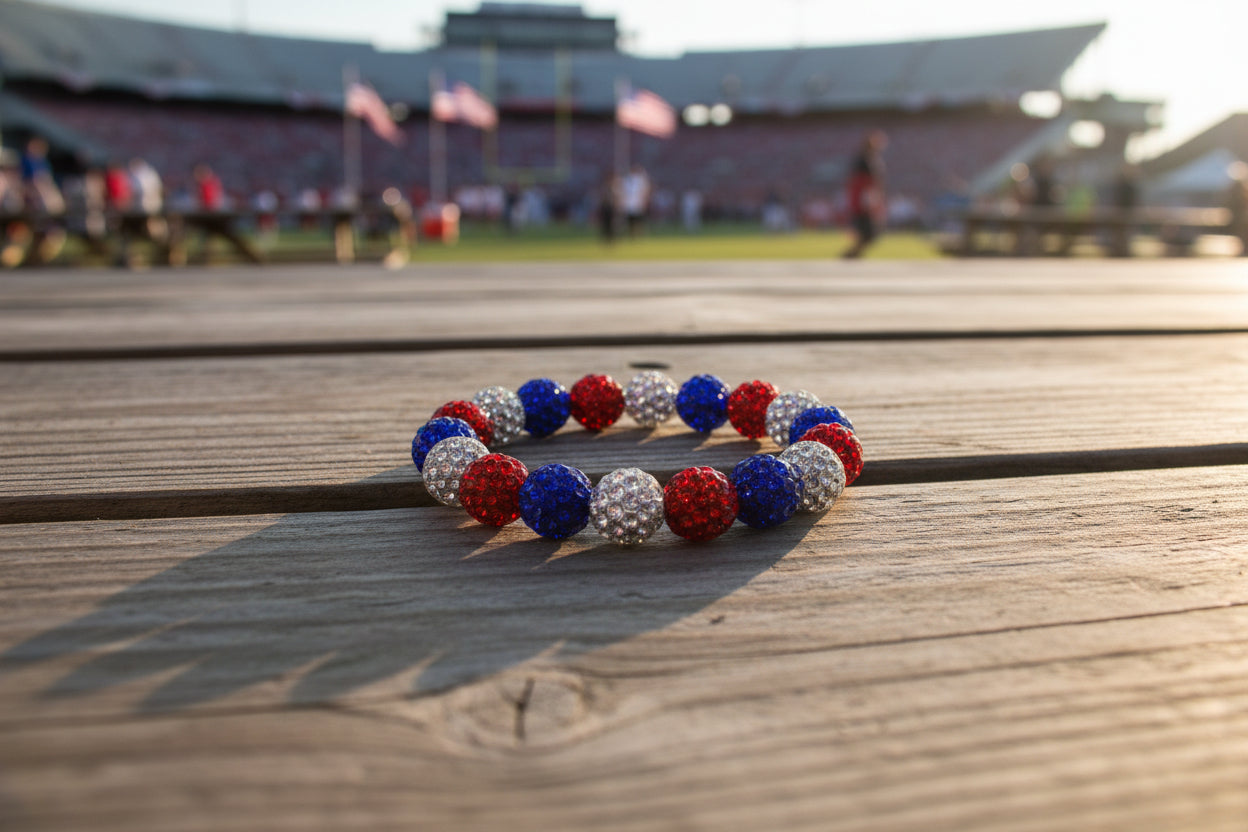 A beaded stretch bracelet featuring alternating red, blue, and silver rhinestone-covered round beads, arranged in a circle on a neutral gray background.