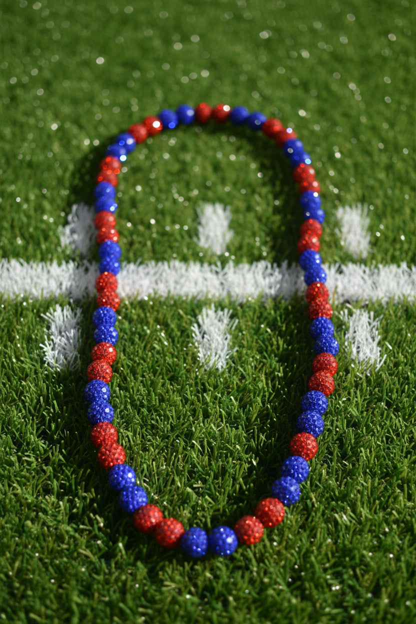 A beaded necklace made of alternating red and blue faceted round beads, laid flat on a light gray background.