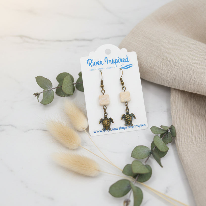 Turtle-themed earrings on a 'River Inspired' branded card against a gray background