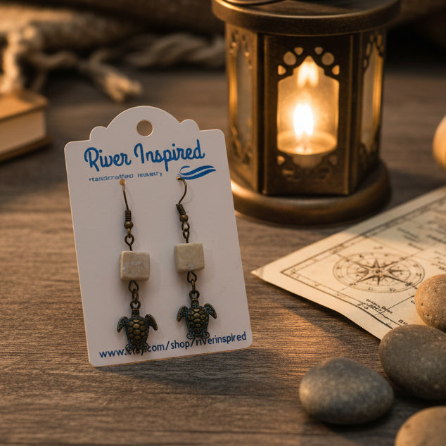 Tortoise-shaped earrings on a 'River Inspired' branded card against a gray background