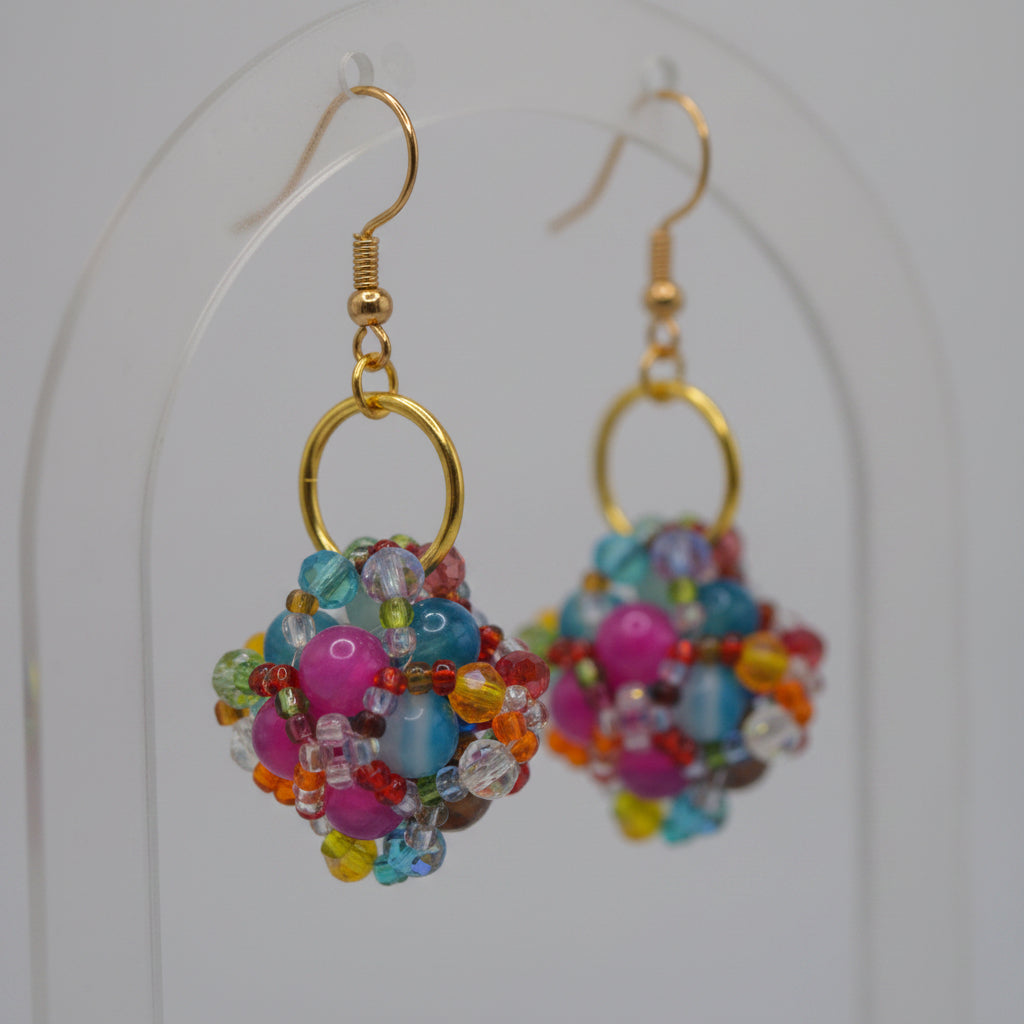 A pair of handmade beaded dangle earrings with gold fishhook wires and colorful glass beads, displayed against a neutral gray background.