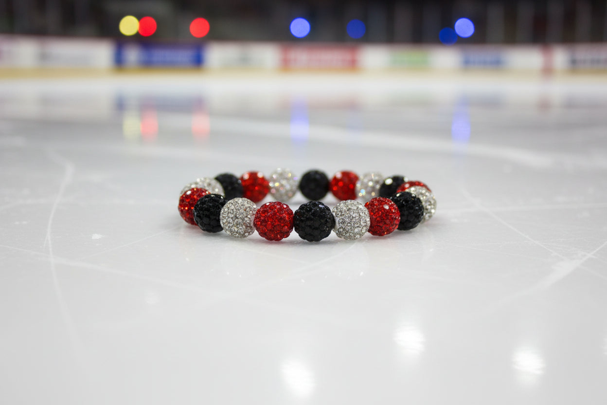 A beaded stretch bracelet featuring alternating red, black, and silver rhinestone-covered round beads, displayed on a neutral light gray background.