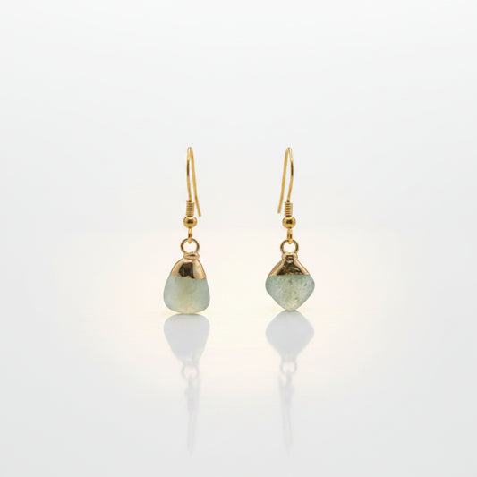 A pair of gold dangle earrings with irregular light green stone pendants, displayed on a clear acrylic stand against a neutral gray background.