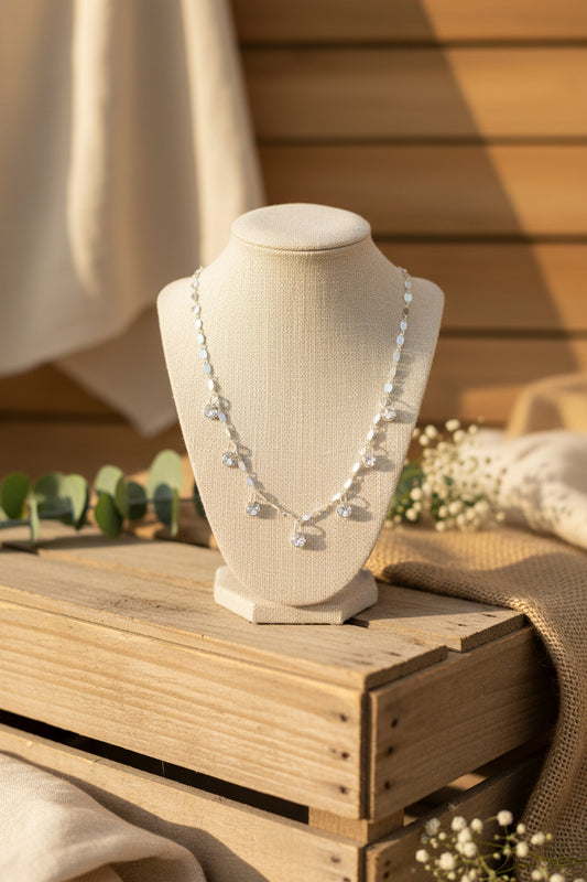 A silver-toned necklace with small dangling charms displayed on a black velvet jewelry bust against a white background.