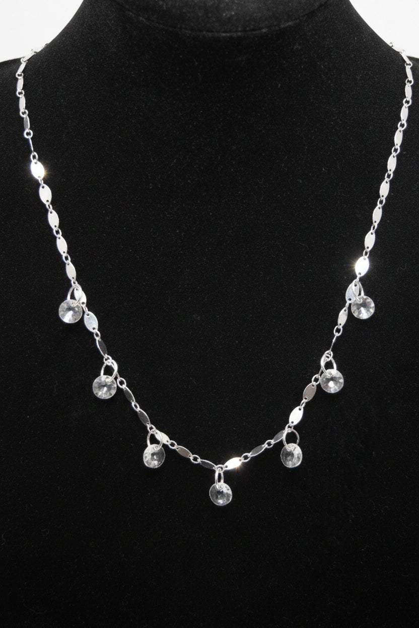 A silver-toned beaded necklace with small dangling charms, displayed on a black velvet jewelry bust against a white background.