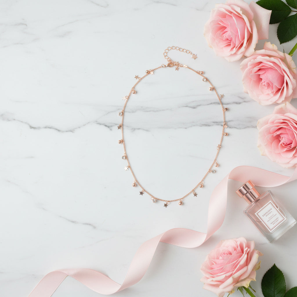 Rose gold necklace with star and bell charms on a gray background