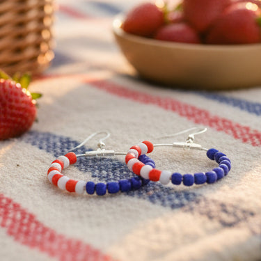 Pair of hoop earrings with red, white, and blue beads on a gray background